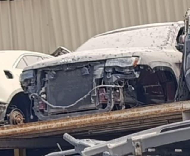 Dusty Jeep Grand Cherokee for parts on a flatbed, bumper removed, showing radiator and headlight, Sharjah market