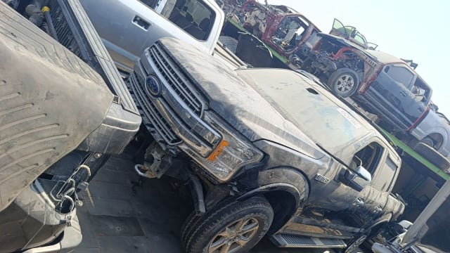 Dusty dark grey Ford F150 pickup for parts — grille, headlight, hood and doors, bumper missing, Sharjah market