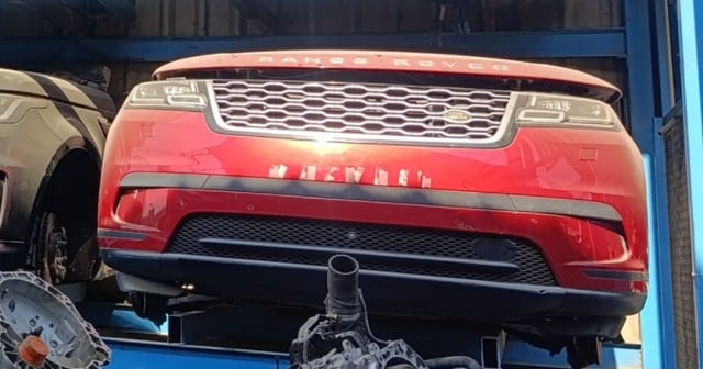 Red Range Rover Velar front halfcut with hood, grille, headlights and bumper on a rack, Sharjah market