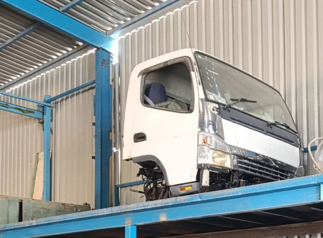 White Mitsubishi Fuso Canter cab halfcut on a rack: door, windshield, headlights and grille, Sharjah market