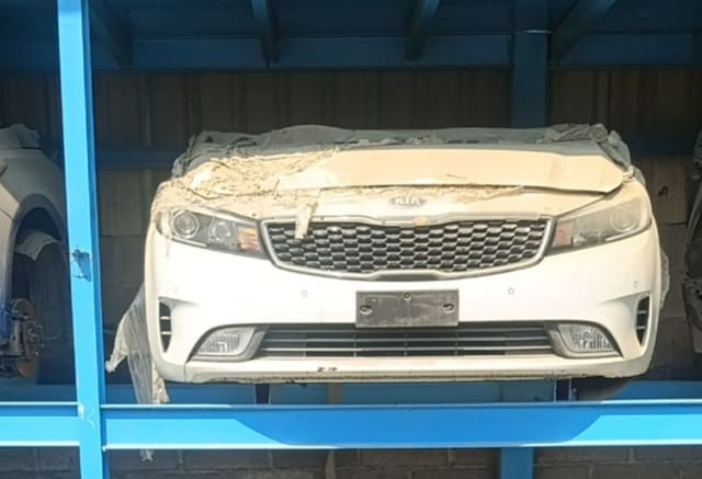 White Kia Cerato front halfcut — bumper, grille, headlights and wrapped hood on rack, Sharjah market