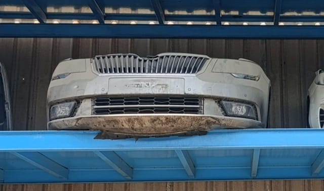 Dusty white Skoda Superb front end on rack: grille, headlights, fog lights and bumper, Sharjah market