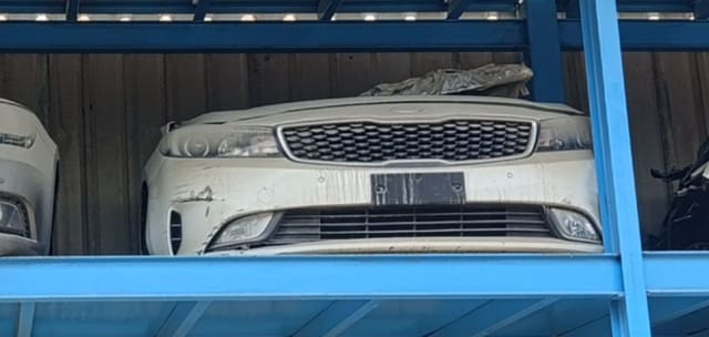 White Kia Cerato sedan front halfcut — bumper, grille, headlights and hood on a rack, Sharjah market