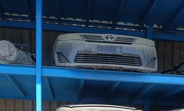 Dusty grey Toyota Camry front bumper with grille and emblem on blue rack, Sharjah market