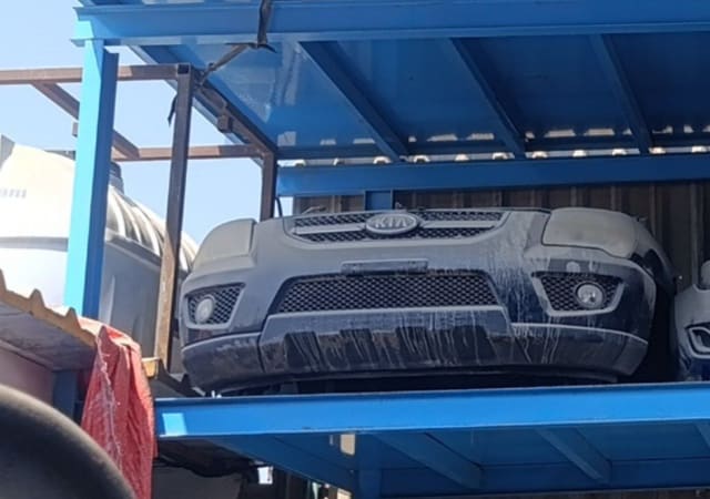 Dark Kia Sportage front halfcut on blue rack: bumper, grille with Kia badge and fog lights, Sharjah market