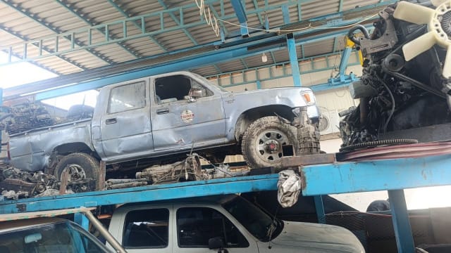 Pale blue Toyota Hilux double cab for parts on a warehouse rack with gearbox nearby, Sharjah market