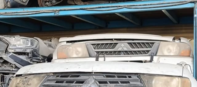 White Mitsubishi Pajero front halfcuts stacked on a shelf — grille, headlights and hood, Sharjah market