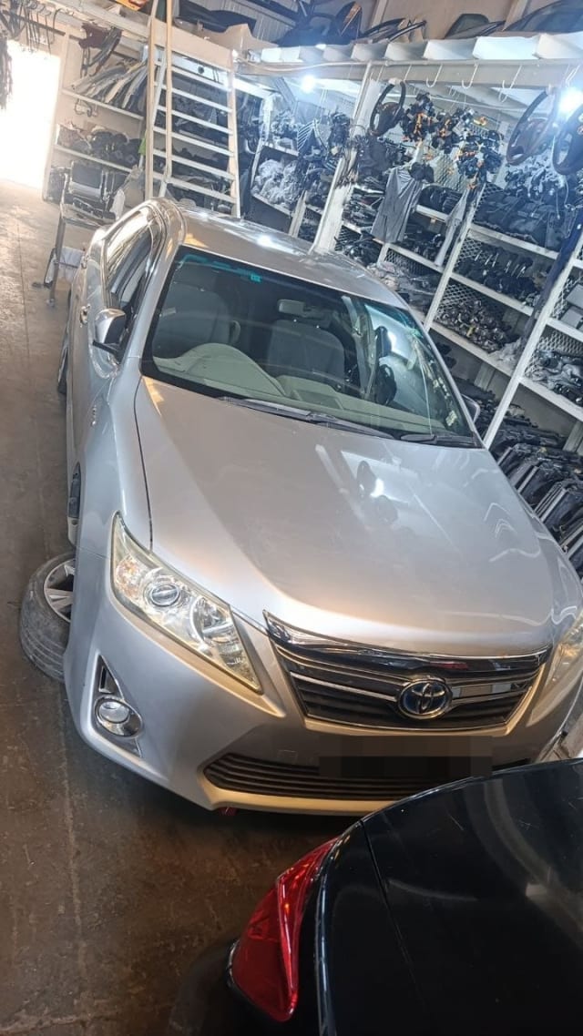 Silver Toyota Camry sedan for parts: hood, grille, headlights and front bumper in a Sharjah parts warehouse