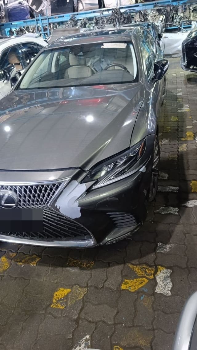 Dark grey Lexus LS sedan, front three-quarter view: hood, headlight, grille, scuffed bumper, Sharjah market
