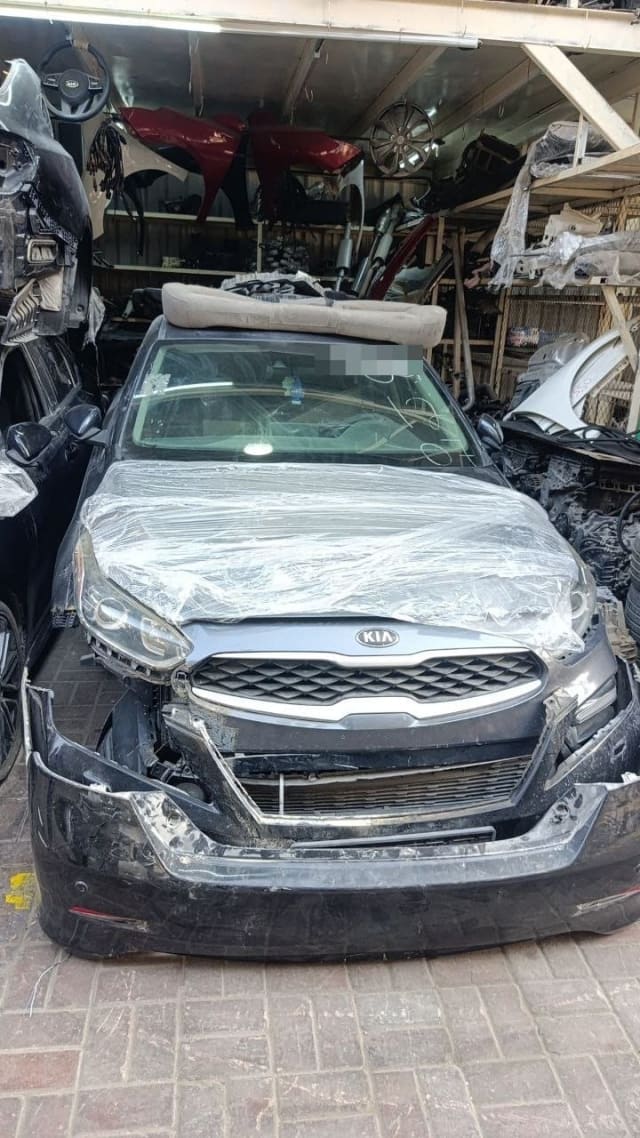 Dark grey Kia halfcut front view: grille, headlights, wrapped hood and damaged bumper, Sharjah market