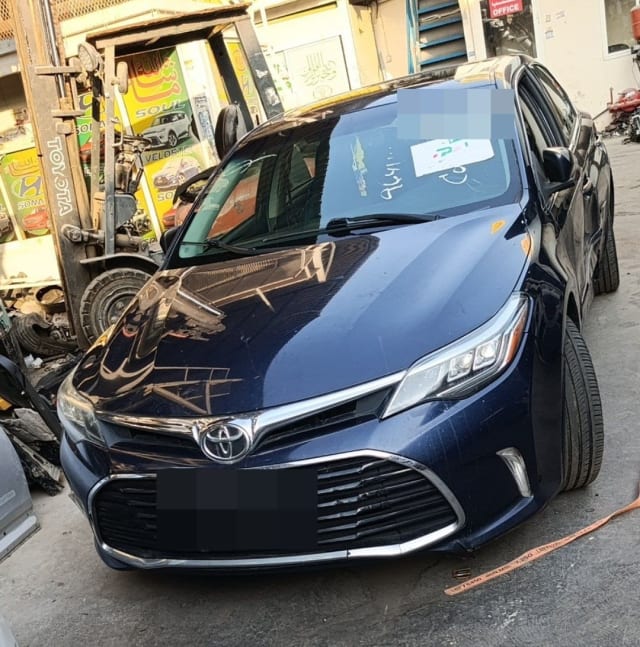 Dark blue Toyota Avalon sedan for parts showing hood, chrome grille and LED headlights, Sharjah market