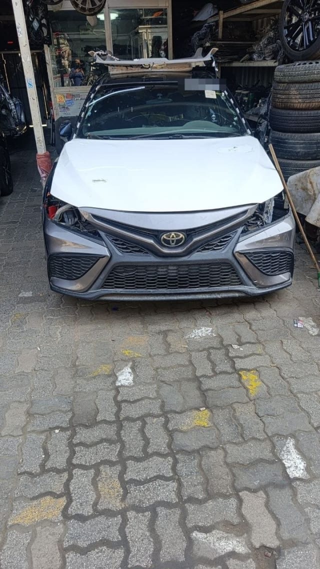 Toyota Camry sedan halfcut front view: white hood, grey bumper and mesh grille, Sharjah market