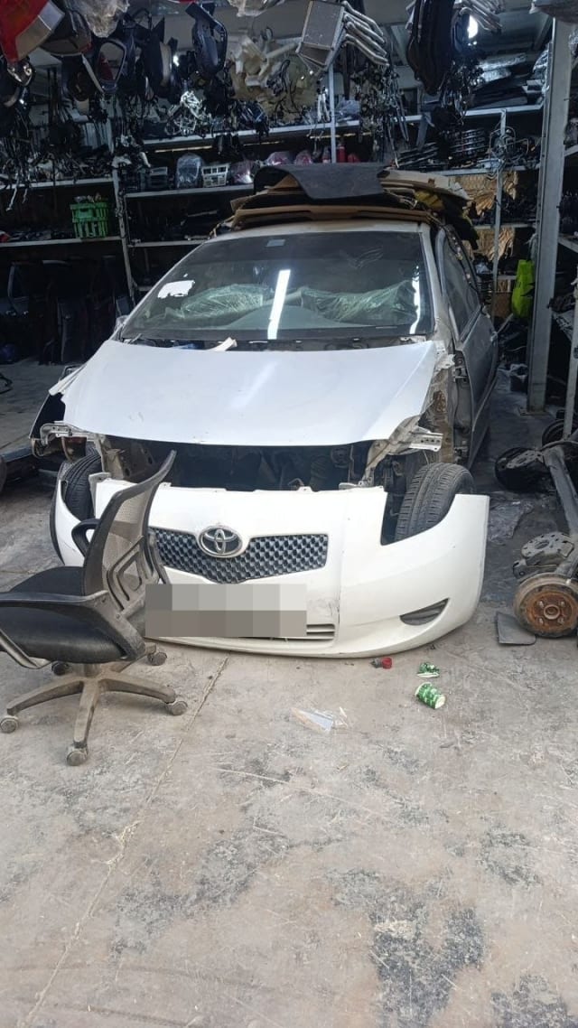 White Toyota Yaris hatchback for parts — hood, bumper and grille, headlights removed, Sharjah market