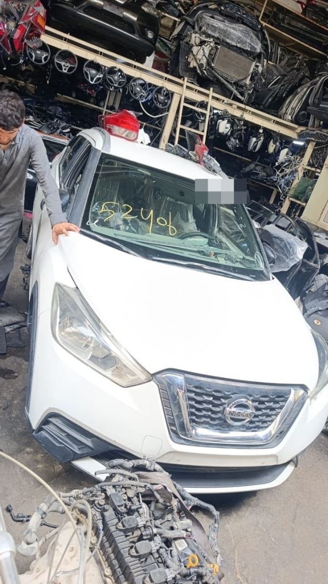 White Nissan Kicks halfcut front view: grille, headlights, hood and bumper, engine beside it, Sharjah market