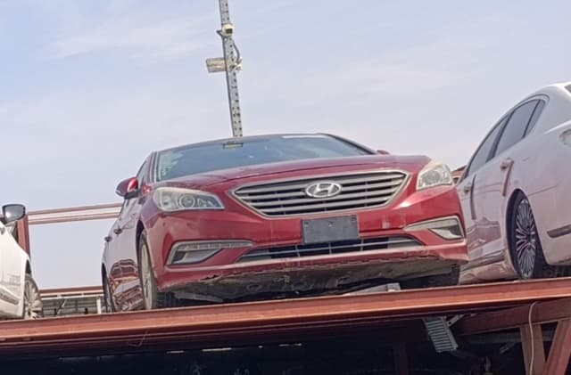 Red Hyundai Sonata sedan for parts on a carrier: front bumper, grille and headlights, Sharjah market