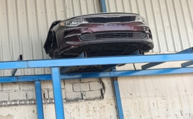 Burgundy Kia Optima front cut on a blue rack with bumper, grille and headlights, Sharjah market