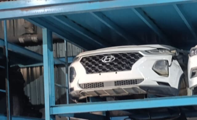 White Hyundai Santa Fe front cut with hexagonal grille, bumper and lights on a rack, Sharjah market