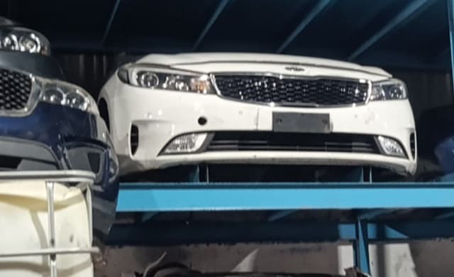 White Kia Cerato sedan front halfcut on blue rack — bumper, grille, headlights, Sharjah market