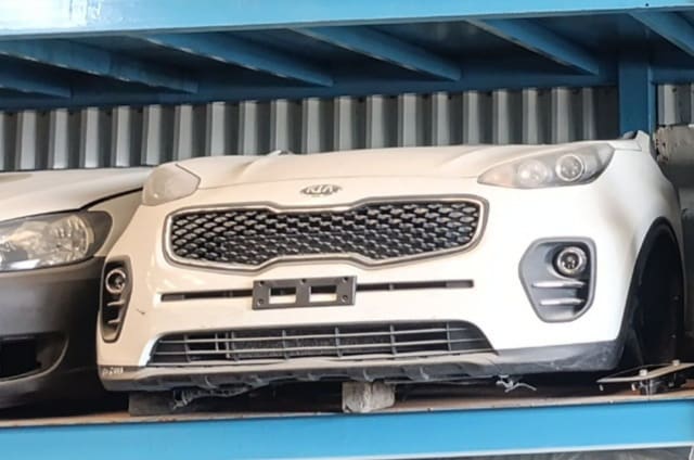 White Kia Sportage front halfcut: bumper, grille, headlights and hood on a rack, Sharjah market