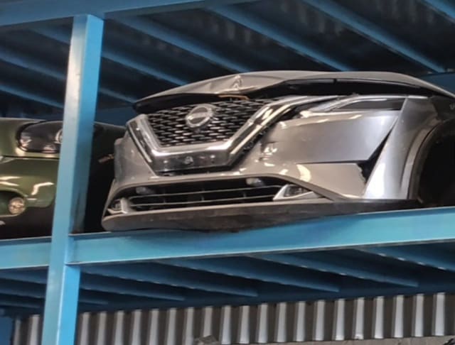 Grey Nissan Qashqai front halfcut on a rack: bumper, chrome grille, headlight and dented hood, Sharjah market