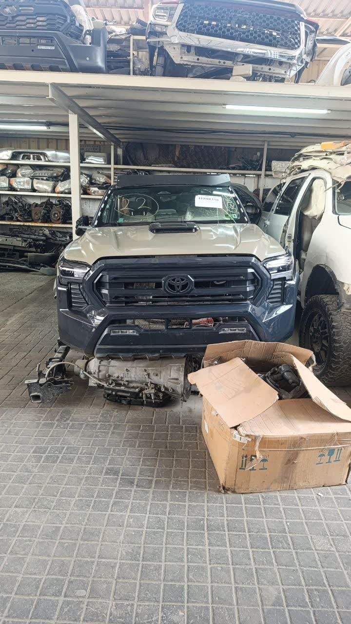 Tan Toyota Tacoma pickup halfcut — hood, grille, headlights, bumper with engine on ground, Sharjah market