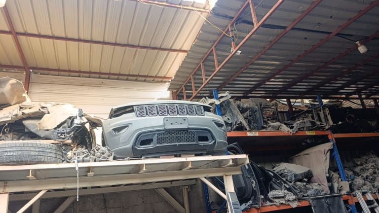 Light grey Jeep Grand Cherokee front halfcut — bumper and seven-slot grille on warehouse rack, Sharjah market