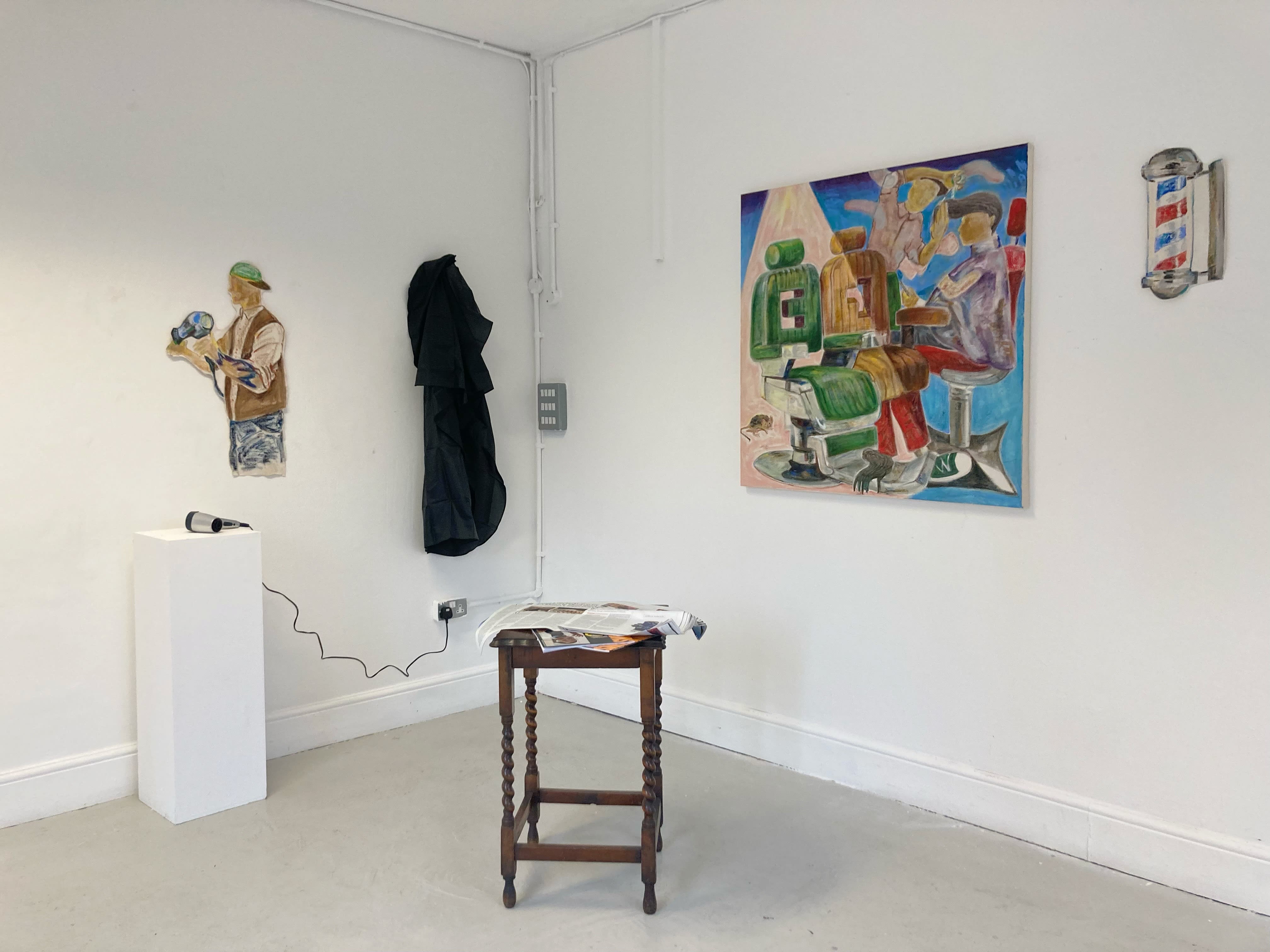 Site specific artwork showing the barbershop painting, along with a barbers cape, a hairdryer, and a stool with some magazines on it