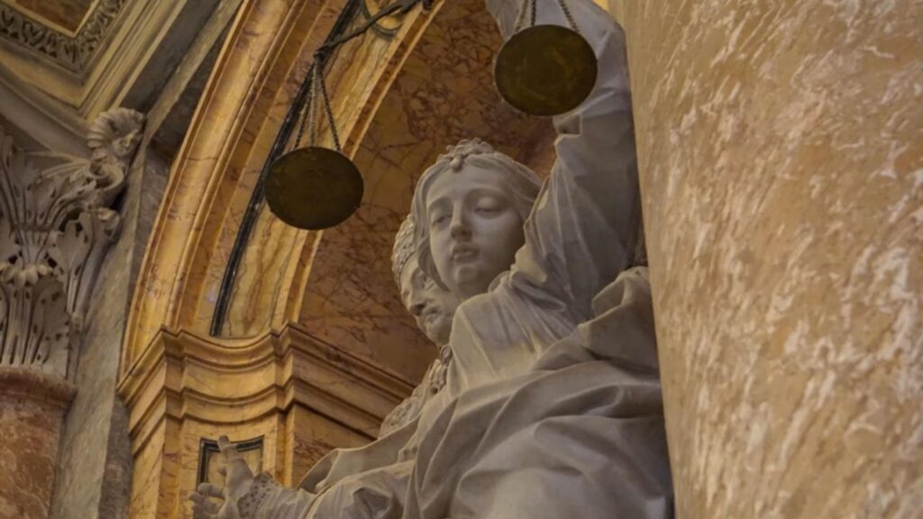 Detailed close-up of a Renaissance marble statue depicting Lady Justice, the ancient Roman goddess Justitia, with scales inside St. Peter’s Basilica at the Vatican. | Credit: Alexander Ruszczynski/Shutterstock