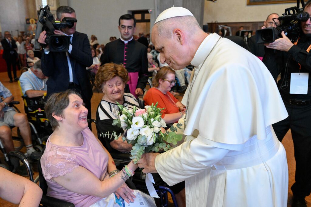 Pope Leo XIV is handed flowers by a woman in a wheelchair at Rimini Cathedral, Aug. 22, 2026, during a meeting with people suffering from illnesses and disabilities. | Credit: Vatican Media