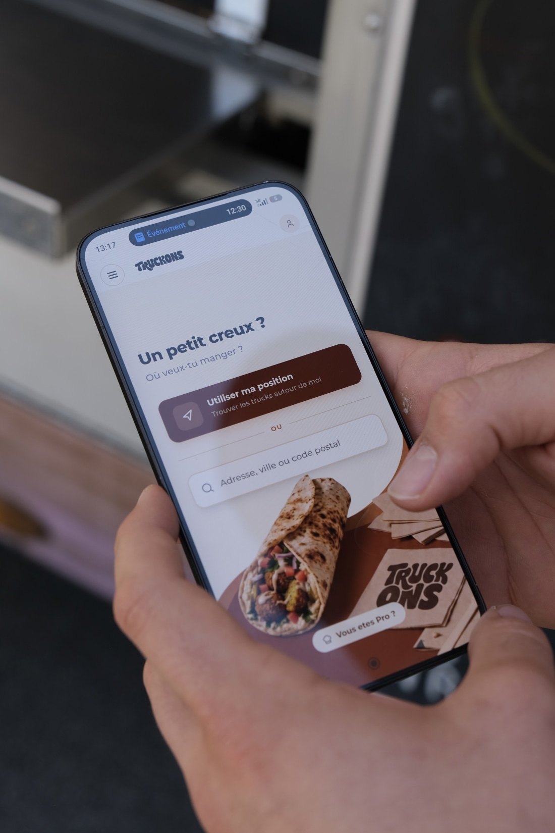 Smartphone affichant l'écran d'accueil de l'app client Truckons « Un petit creux ? Où veux-tu manger ? » avec un wrap appétissant en illustration