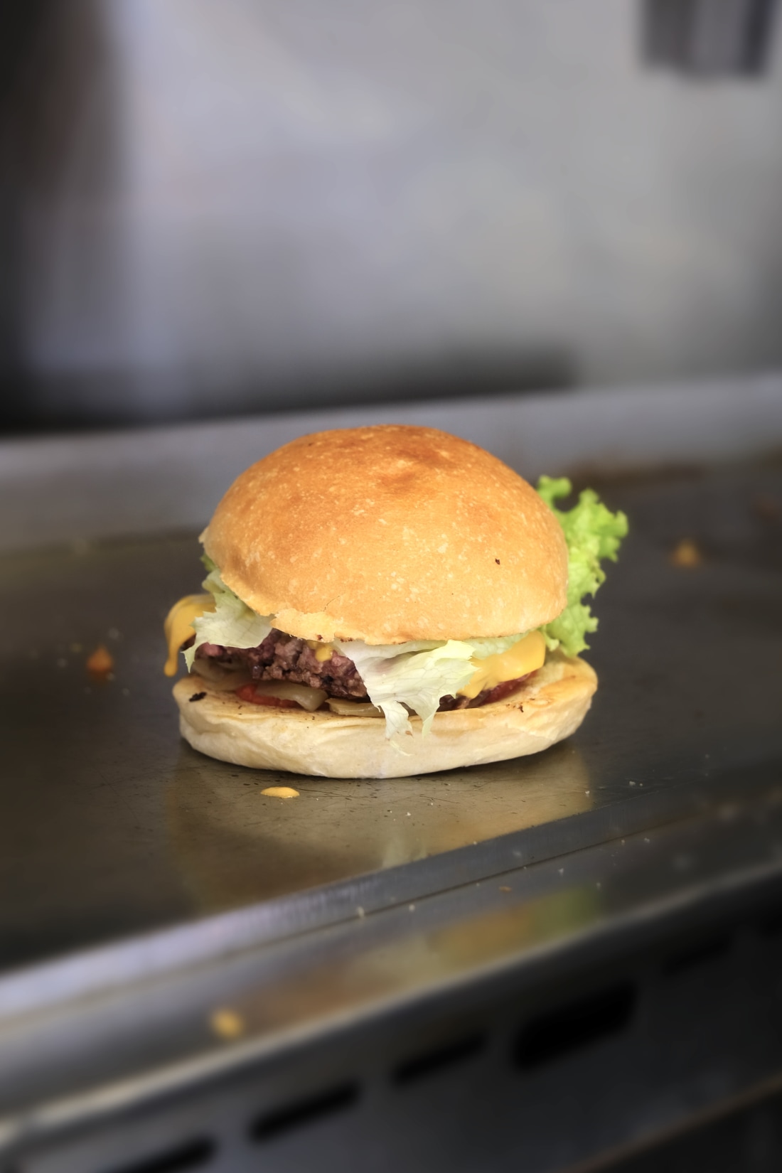 Un burger fait maison sur plaque inox, bun doré, cheddar fondu, salade verte fraîche — l'un des plats signature de La Gamelle