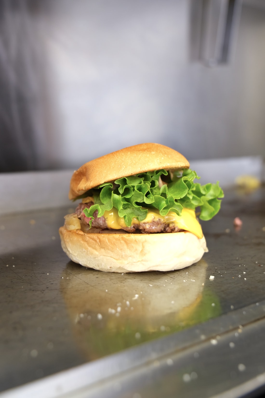 Un smash burger fait maison sur plaque inox, bun doré, cheddar fondu, salade verte croquante, dressage minute