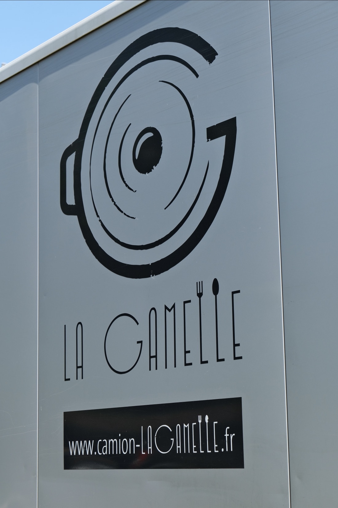 Logo La Gamelle sur le flanc du camion : une marmite stylisée avec un G en arc, identité visuelle blanche sur fond sombre