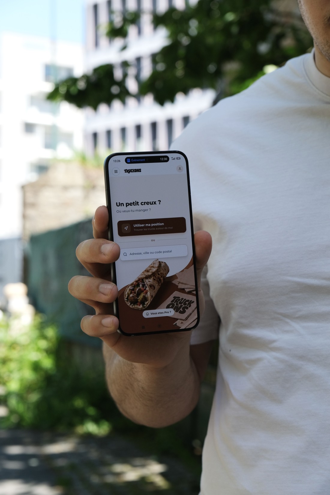 Un homme tient un smartphone qui affiche l'app Truckons en extérieur, écran 'Un petit creux ? Découvrez les food trucks rennais'
