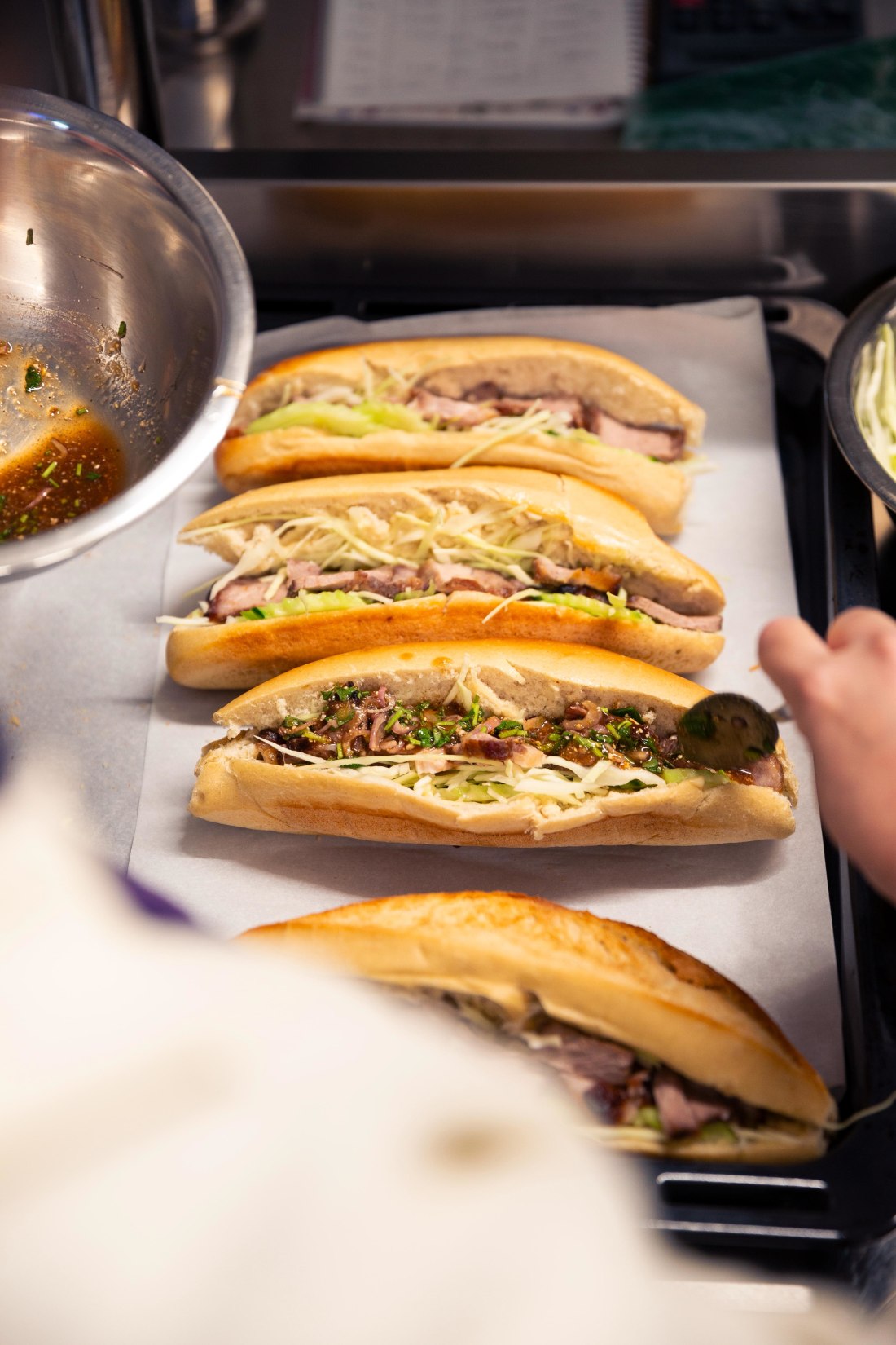 Rangée de bánh mì Banh Banh en cours d'assemblage sur le plan de travail du camion, garnitures variées et coriandre