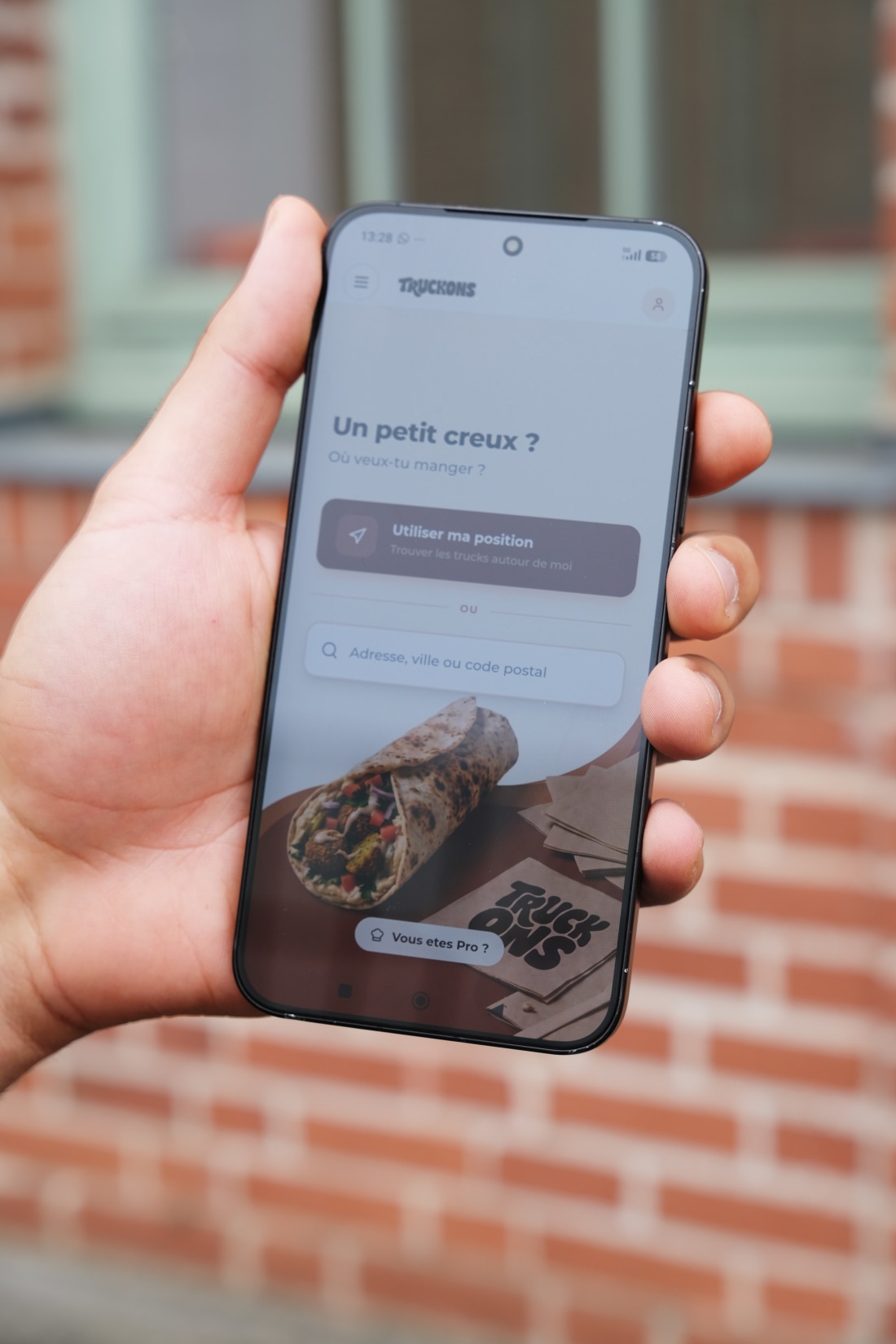 Une main tenant un smartphone qui affiche l'application Truckons pour commander dans un food truck