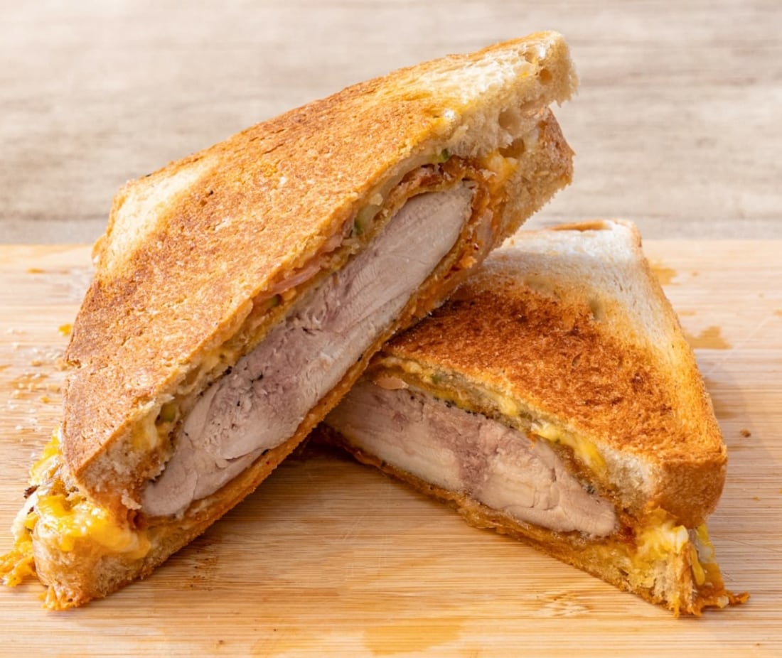 Un grilled cheese au poulet frit de Makdus coupé en deux, pain de mie doré et croustillant, blanc de poulet pané fondant et fromage filant à l'intérieur