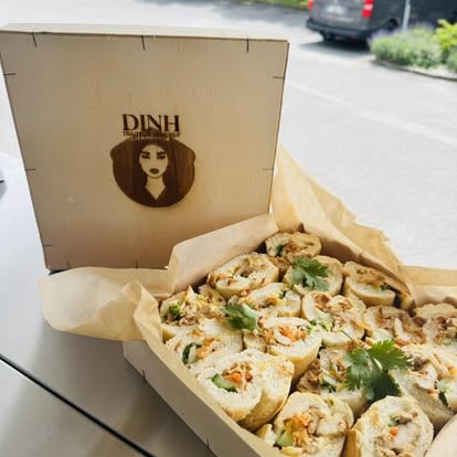 Une « Bánh Mì Box » DINH : une baguette vietnamienne garnie, roulée et tranchée en bouchées, présentée dans une boîte en bois gravée au logo DINH