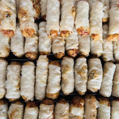 Des dizaines de nems et samoussas vietnamiens dorés, alignés sur des grilles, prêts pour une commande traiteur DINH