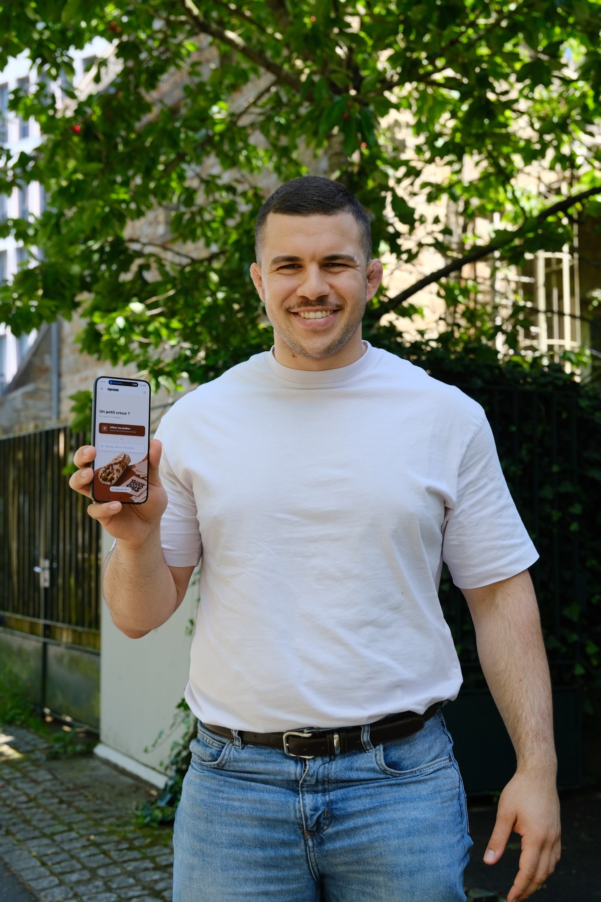 Radwan Joalland, fondateur de Truckons, en extérieur, l'app ouverte sur son téléphone, prêt à aller voir un food truck