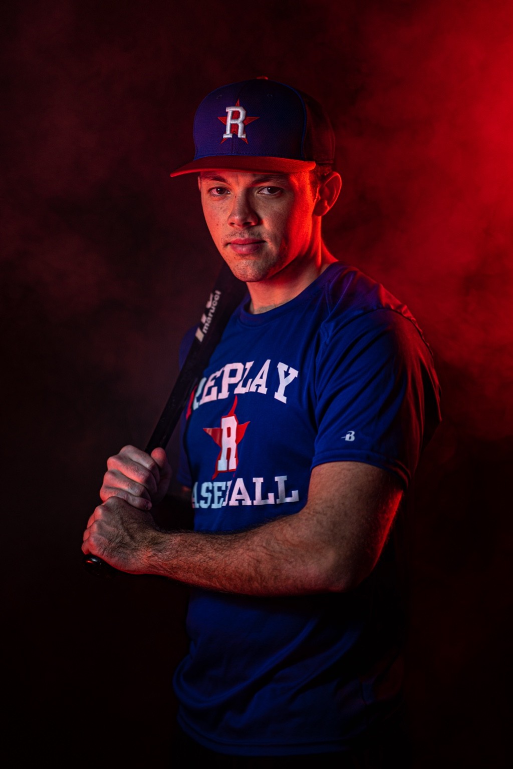 Replay Sports baseball player holding a bat with smoke and red accent lights in Ashburn VA — studio sports portrait photography