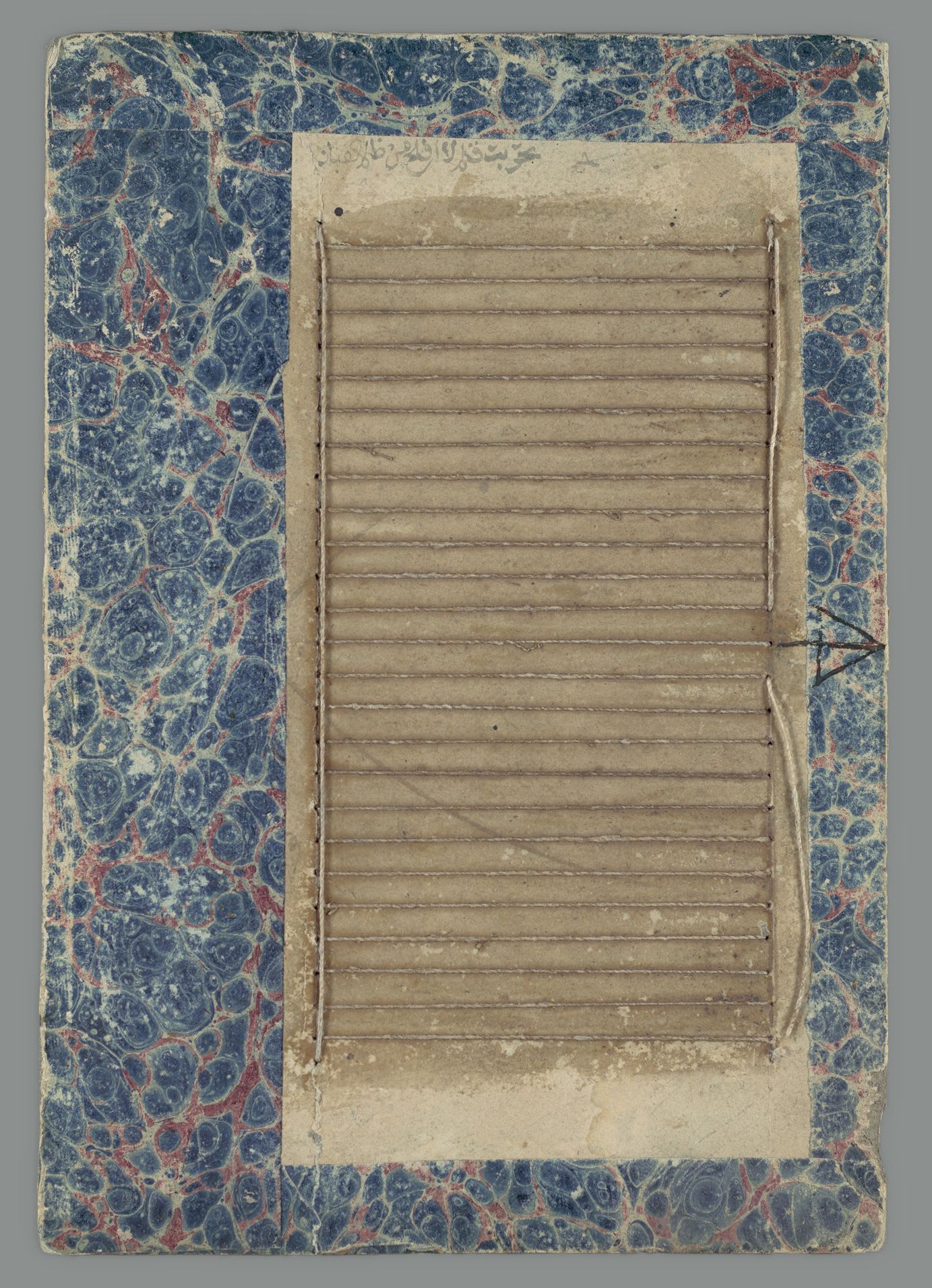 A worn ruling board with parallel cotton strings stretched across its paper surface, surrounded by blue marbling. The complete museum photograph sits toward the right of a wider canvas.