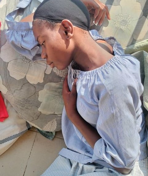 Moreen, fifteen, lying on her side with her eyes closed, her head resting against a floral cushion and one hand drawn up to her chest.