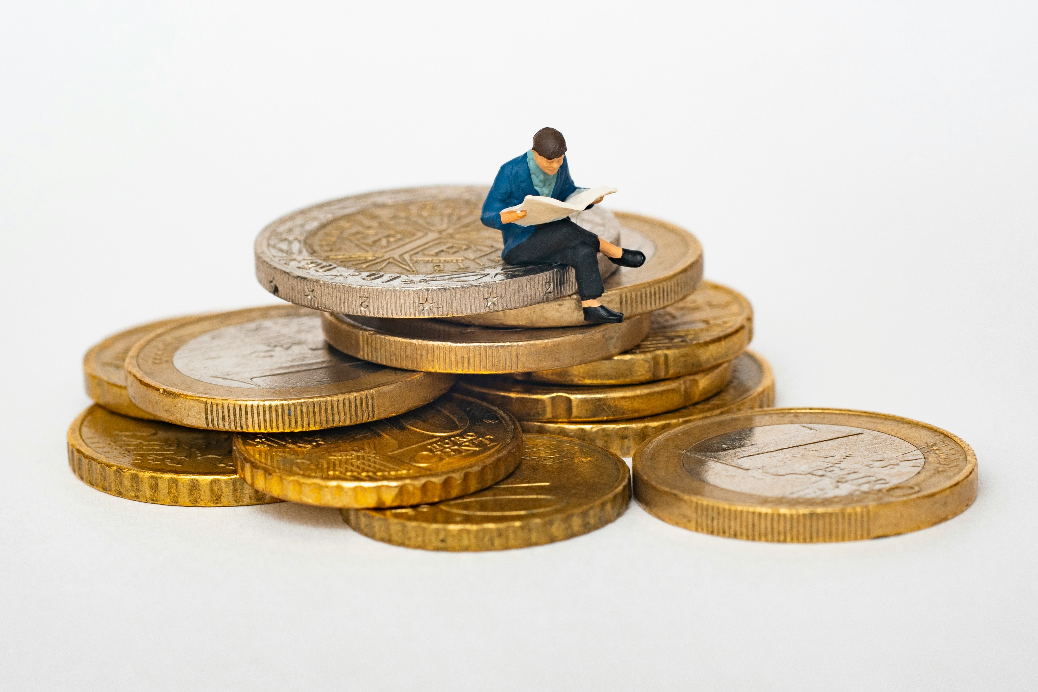 A small figurine of a man reading a newspaper sitting on top a pile of coins