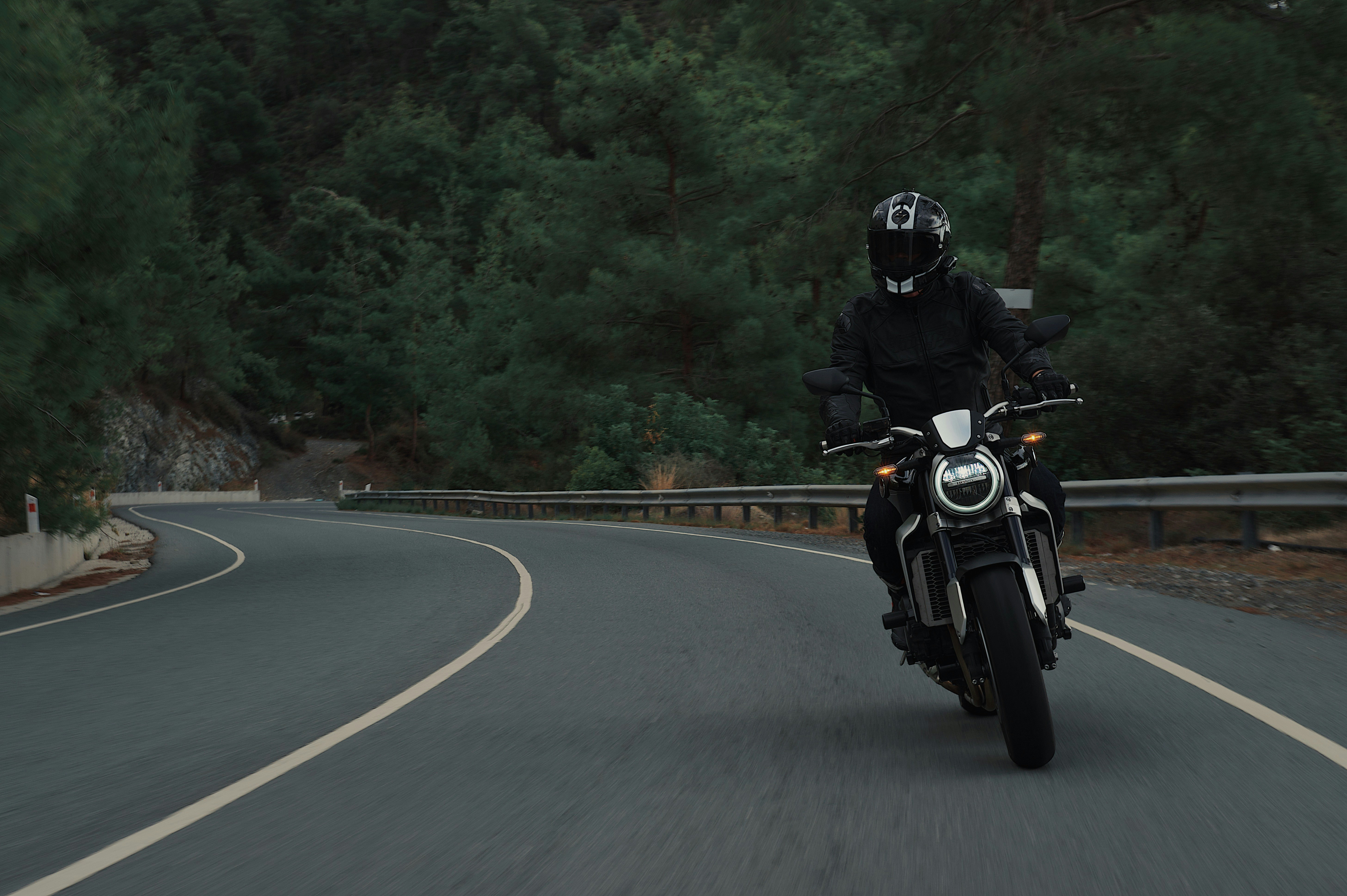 person wearing all black and helmet riding motorcycle down forested road