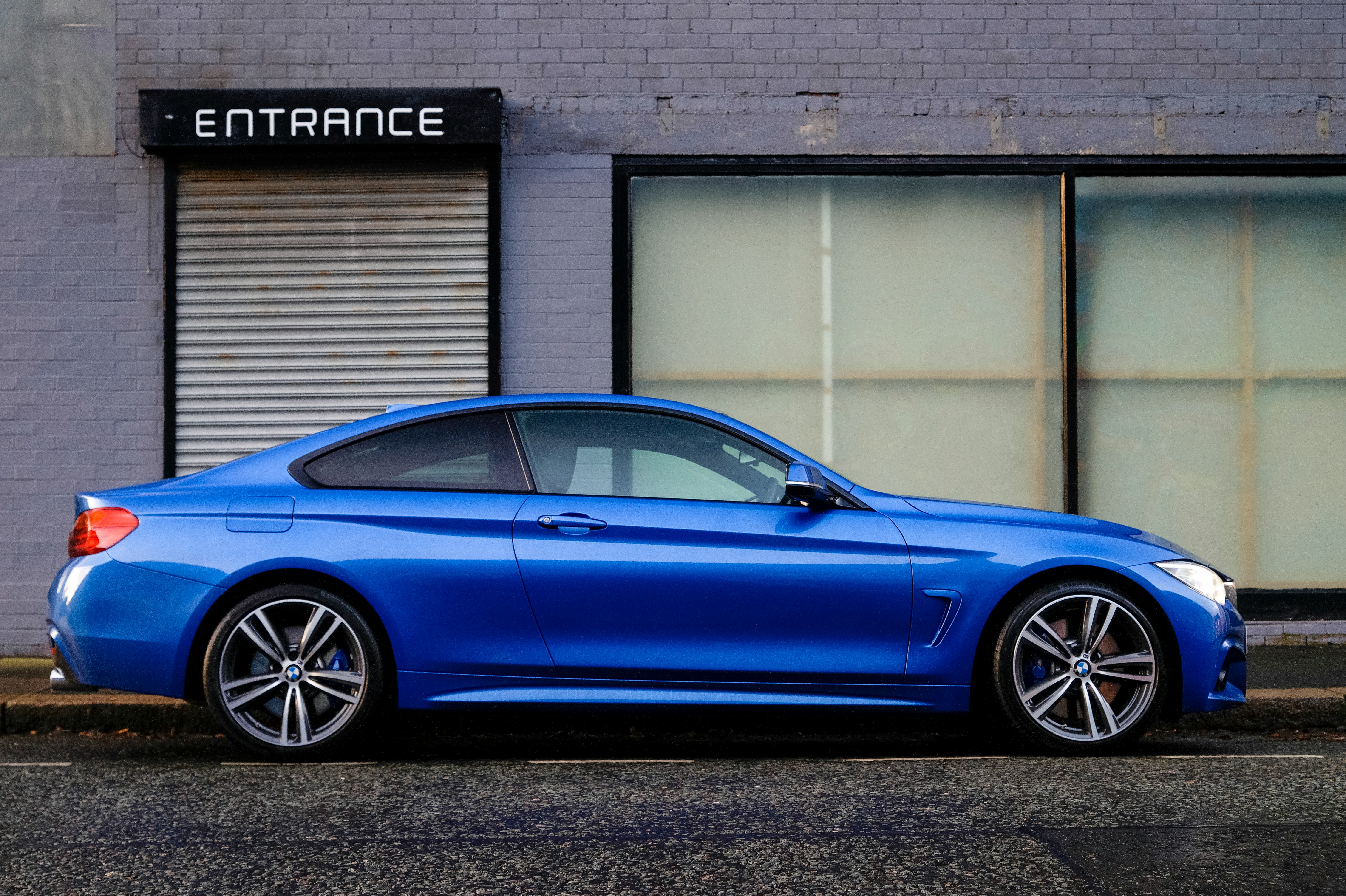 a blue sedan parked in from of a painted brick wall with large windows and an entrance sign