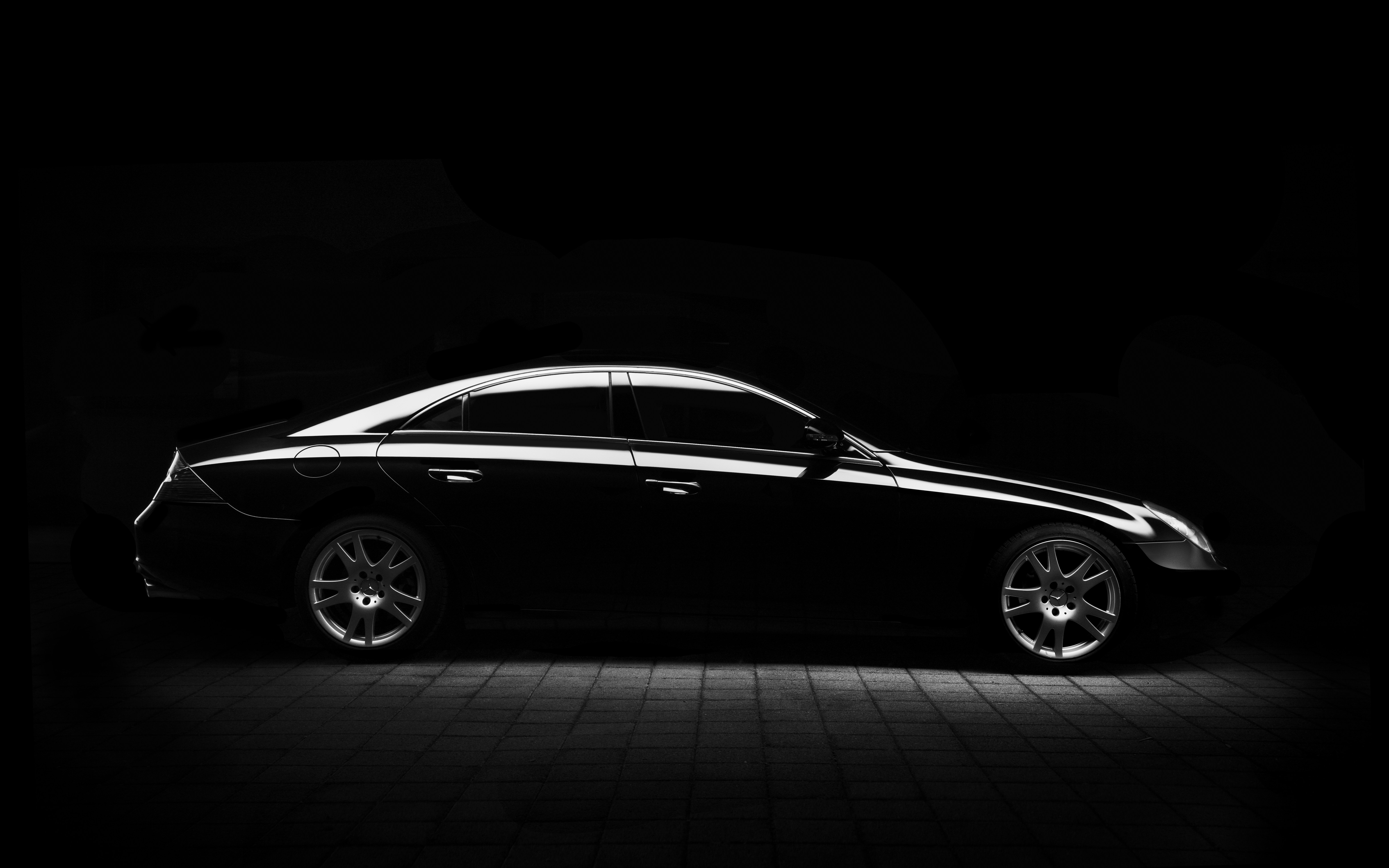 A black car barely illuminated in an all-black space with grey stone floors