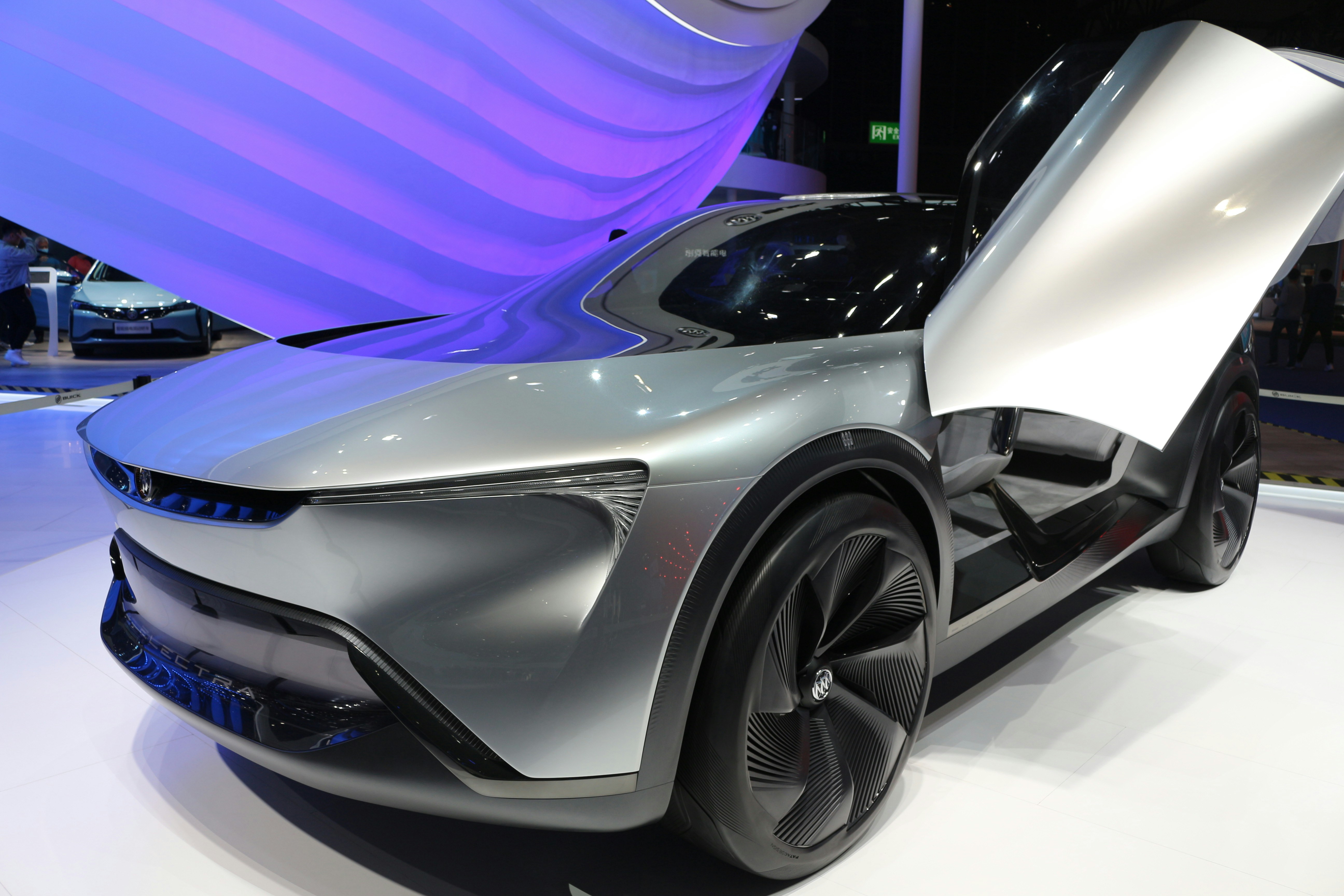 Futuristic silver sedan at expo with a raised butterfly door