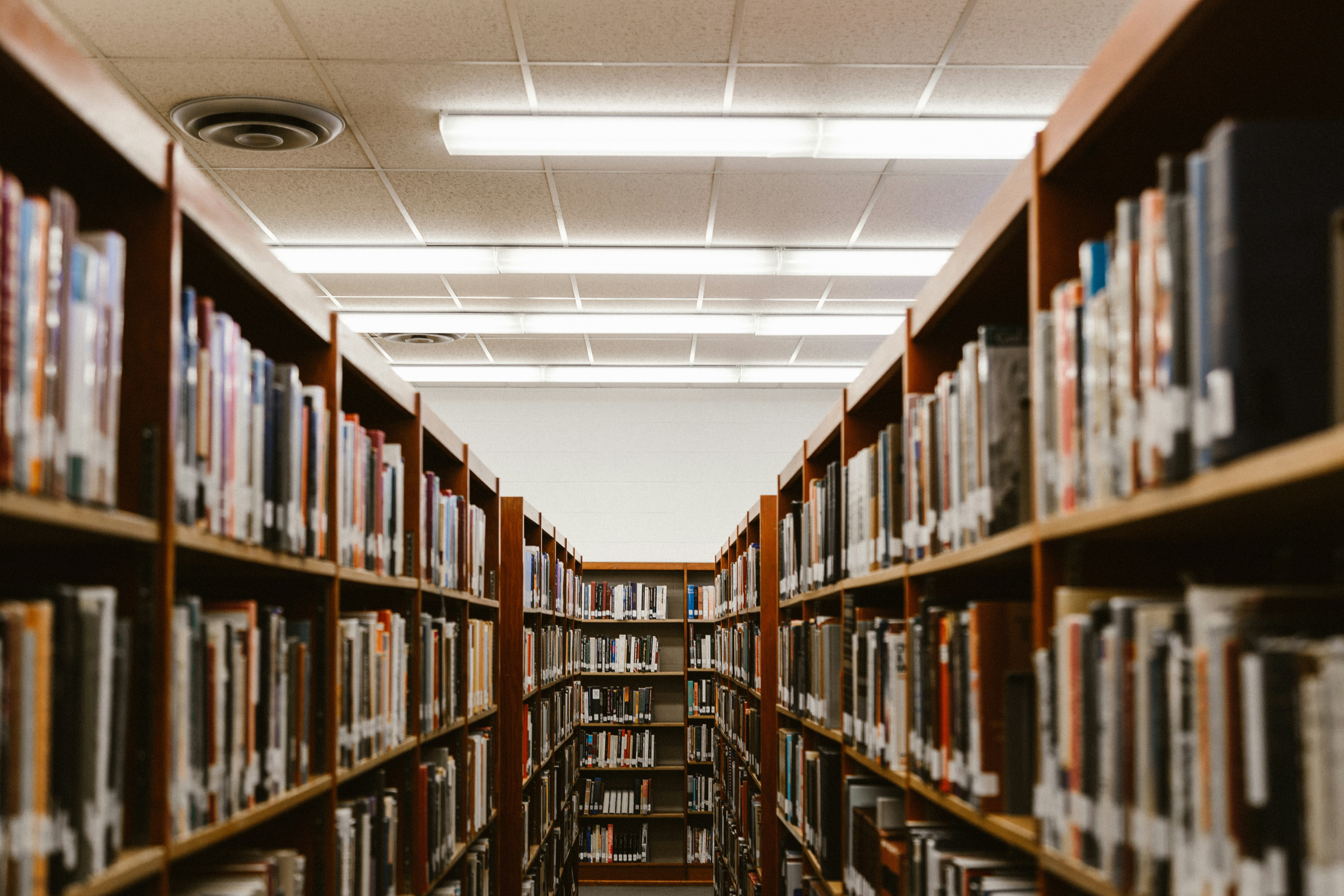 The aisle of a college library with wooden shelves, full of academic books