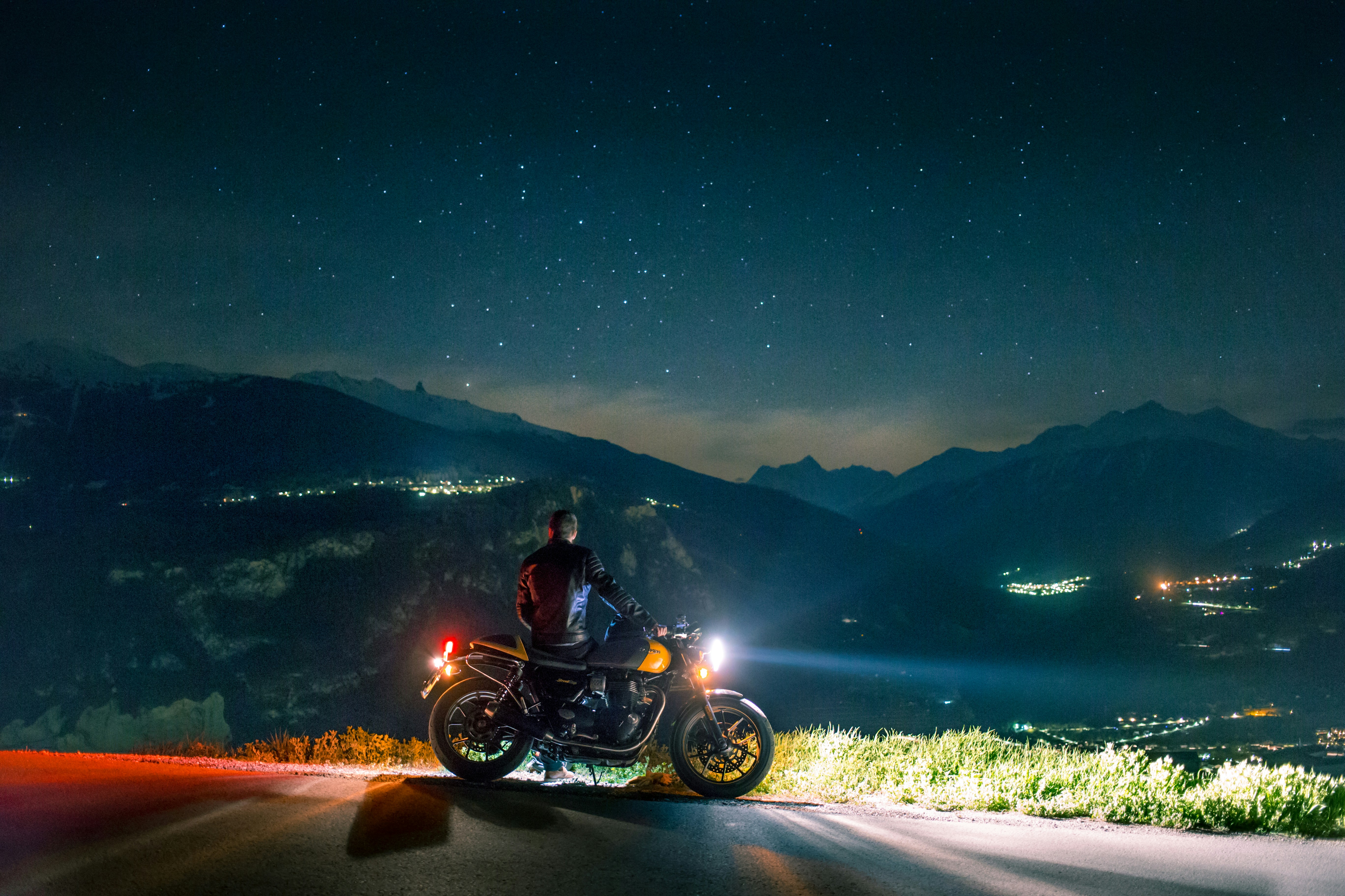 Man leaning on motorcycle parked at top of hill at night